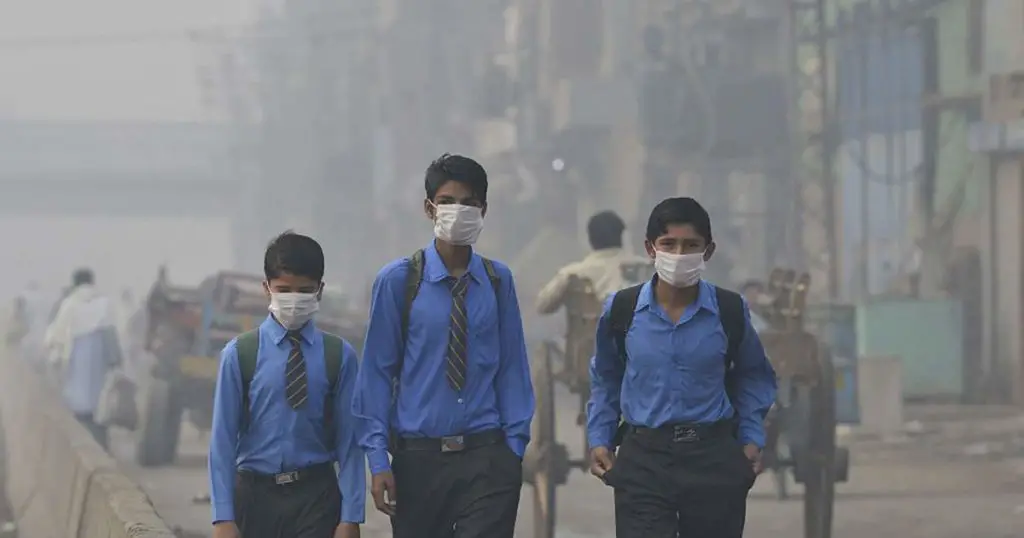 Air pollution in Pakistan. Three boys with face masks are walking down a polluted road.